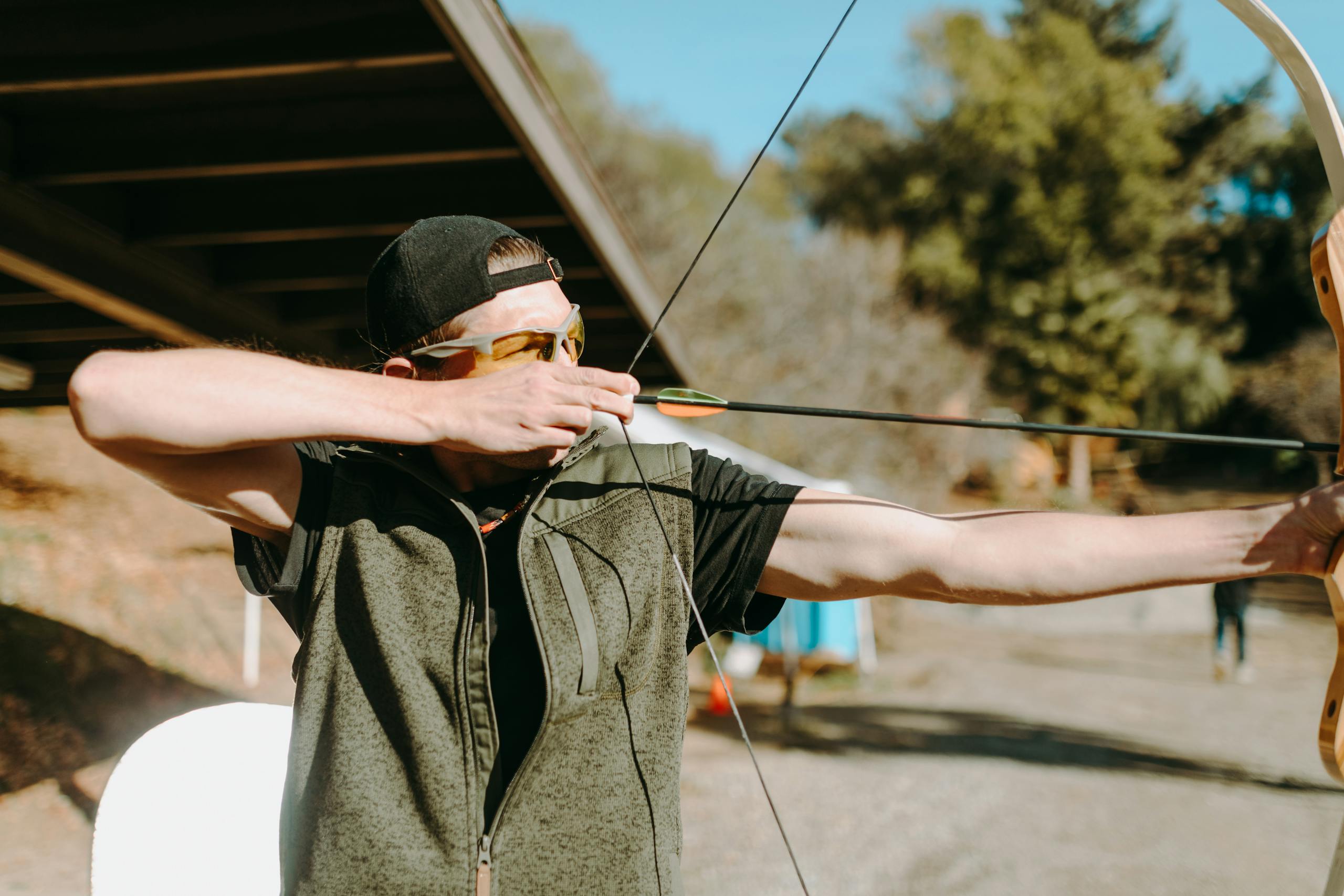 A man aiming a bow and arrow in an outdoor archery range, focusing on the target.