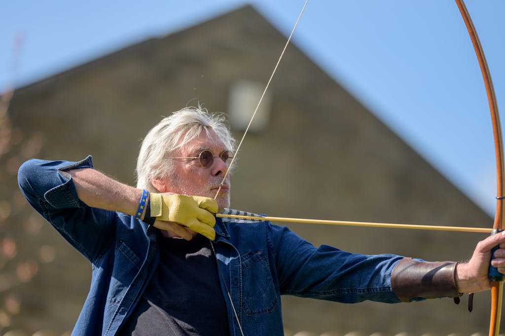 Elderly man aiming a bow and arrow outdoors, showcasing focus and concentration.