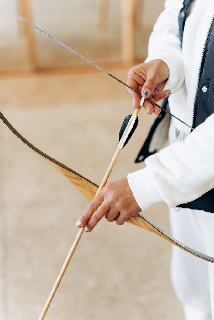 Focused shot of a woman aiming with a bow and arrow indoors, showcasing precise archery skills.